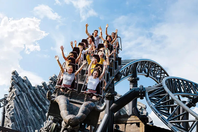 Teenagers riding the Taron roller coaster at Phantasialand, arms raised